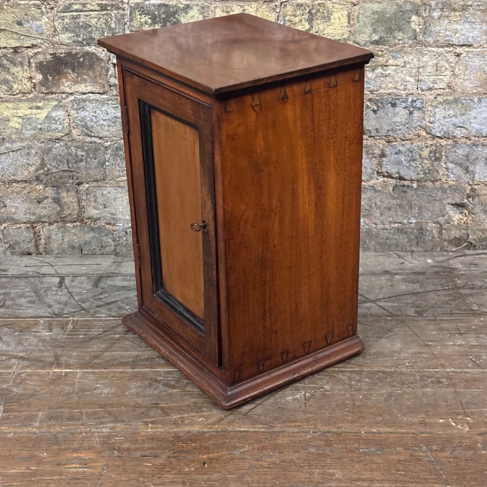 A compact dark mahogany tabletop cabinet featuring a single recessed panel door with a keyhole, a slanted top, and a stepped plinth base. View IV