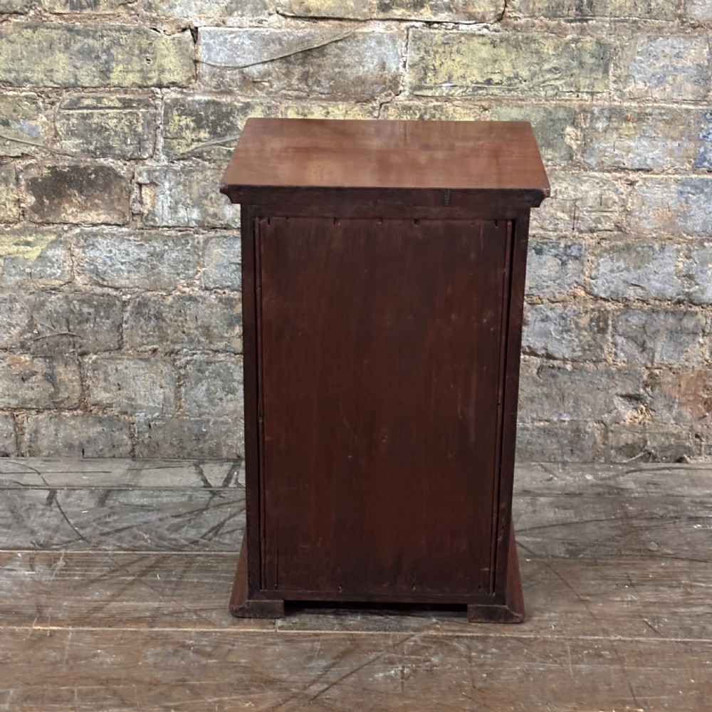 A compact dark mahogany tabletop cabinet featuring a single recessed panel door with a keyhole, a slanted top, and a stepped plinth base. View V