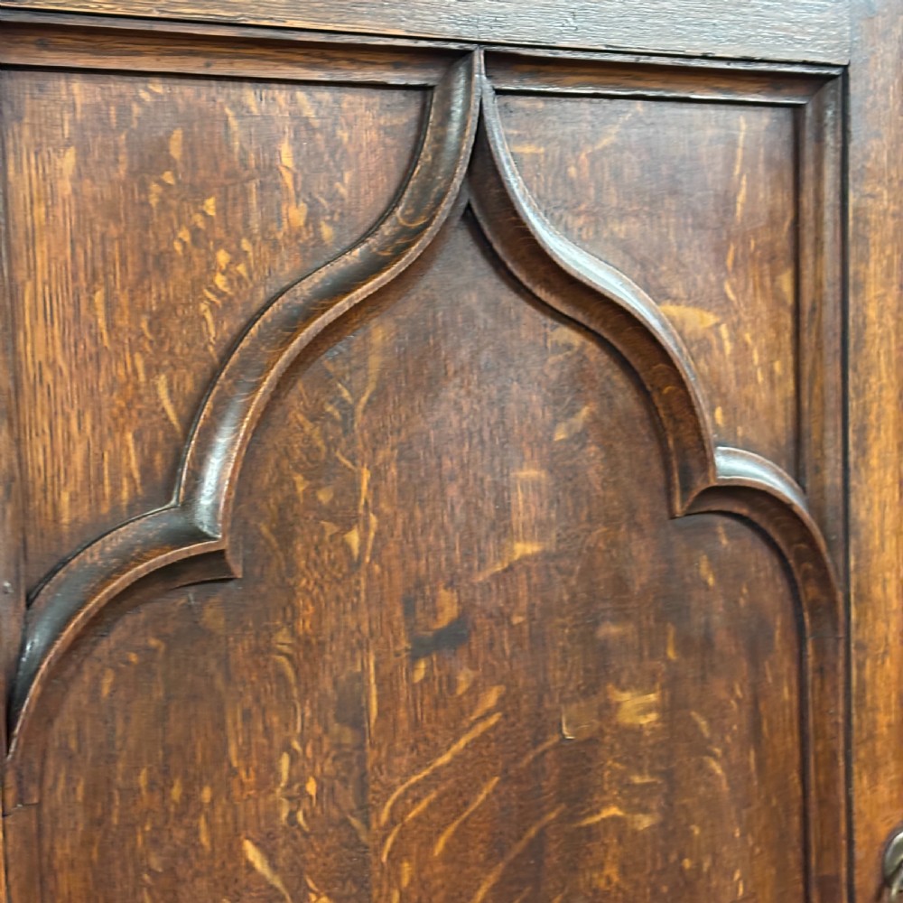 A late Victorian oak cabinet with pointed Gothic arch moulding on two upper panelled doors, two middle drawers, and a lower double-door cupboard. View V