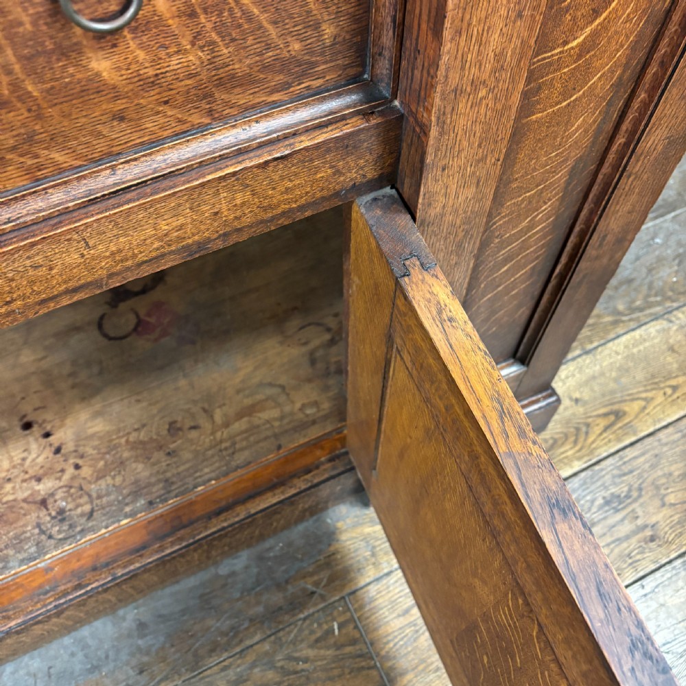 A late Victorian oak cabinet with pointed Gothic arch moulding on two upper panelled doors, two middle drawers, and a lower double-door cupboard. View VII