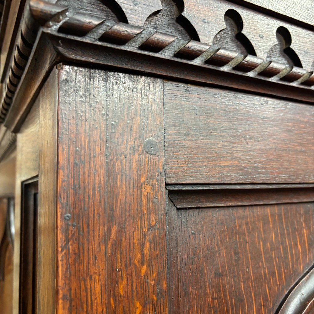 A late Victorian oak cabinet with pointed Gothic arch moulding on two upper panelled doors, two middle drawers, and a lower double-door cupboard. View X
