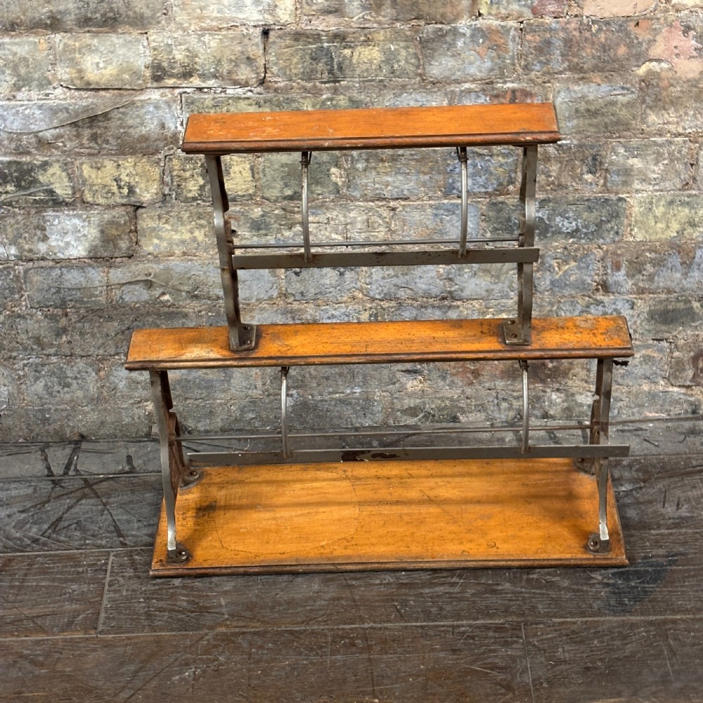 A two-tier antique paper roll dispenser featuring warm brown wooden shelves supported by cast metal side brackets and spring bars.