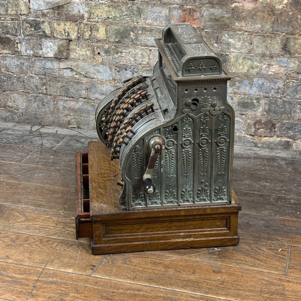 An early twentieth-century mechanical cash register featuring a cast metal case on a wooden base with an open currency drawer. View IV