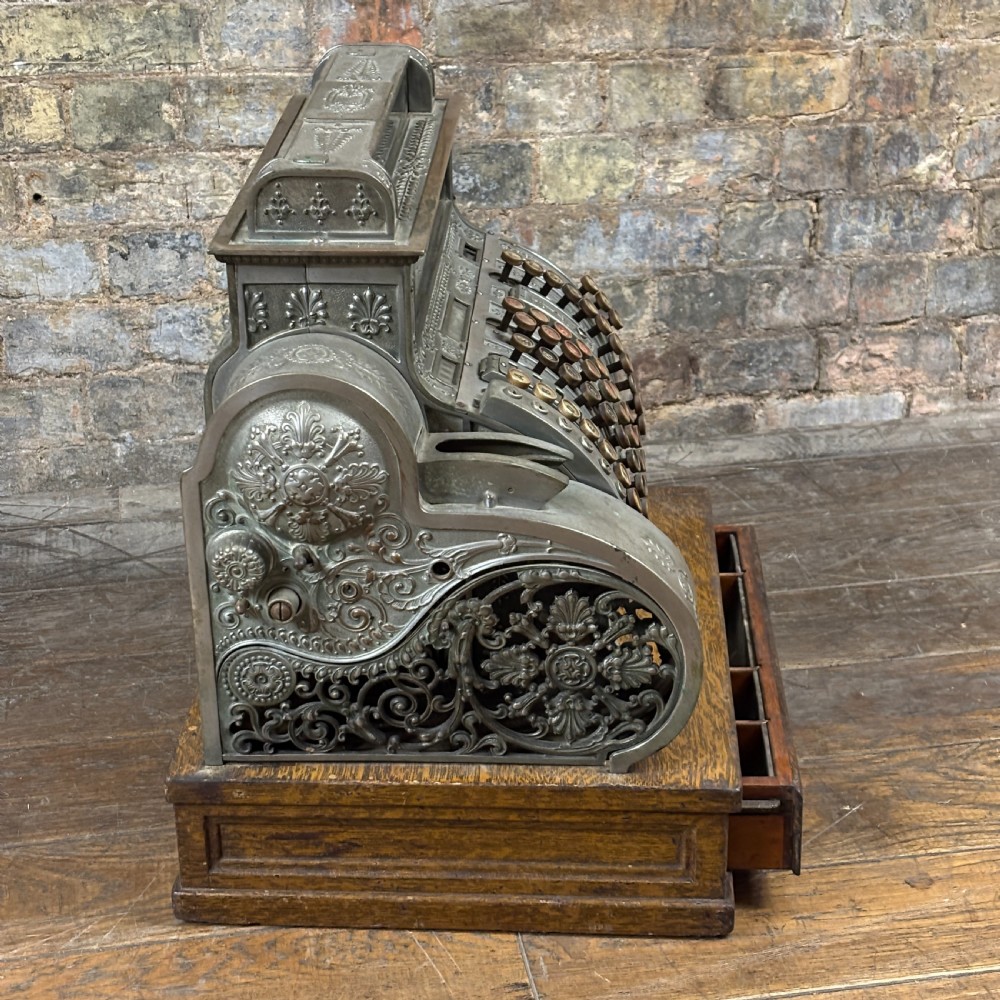 An early twentieth-century mechanical cash register featuring a cast metal case on a wooden base with an open currency drawer. View V