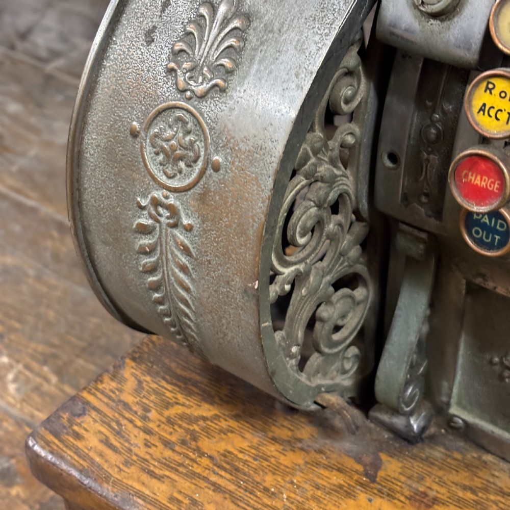 An early twentieth-century mechanical cash register featuring a cast metal case on a wooden base with an open currency drawer. View VI