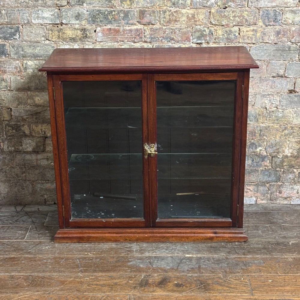 A 1920s dark oak countertop display cabinet featuring twin glazed doors with a central brass catch and internal shelving.