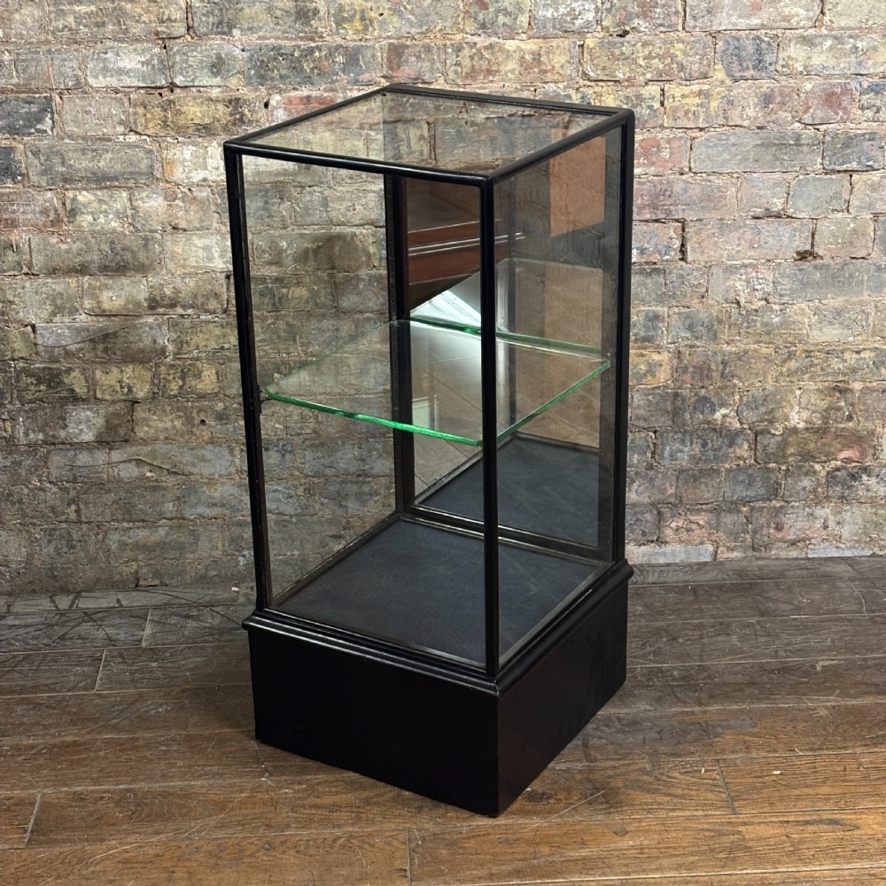 A vertical ebonised wooden countertop display cabinet featuring glazed sides, a central glass shelf, and a mirrored back.