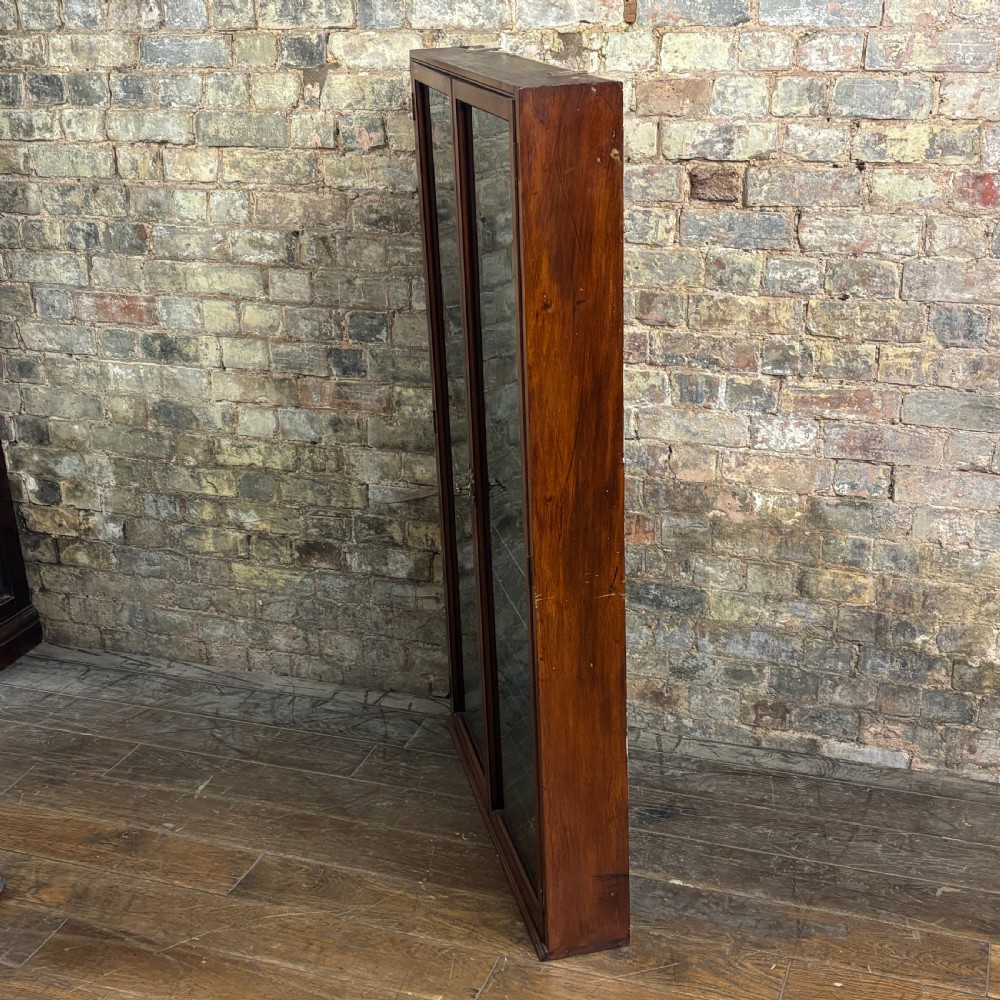 An early 20th-century wall-mounted mahogany cabinet featuring double glazed doors enclosing numerous glass shelves with brass fittings. View V