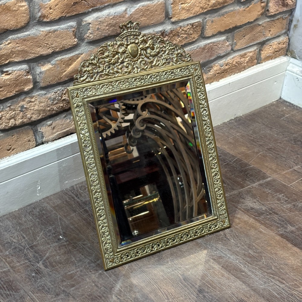 An ornate late nineteenth-century French brass table mirror featuring a crowned crest, relief scrollwork border, and a rectangular bevelled glass plate.