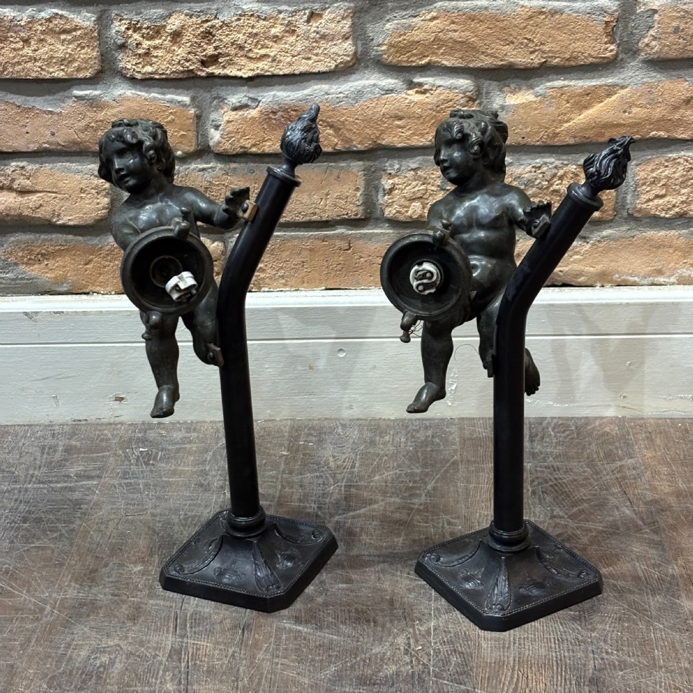 A pair of dark patinated bronze torchere table lamps featuring sculpted cherub figures mounted on decorative square bases. View II