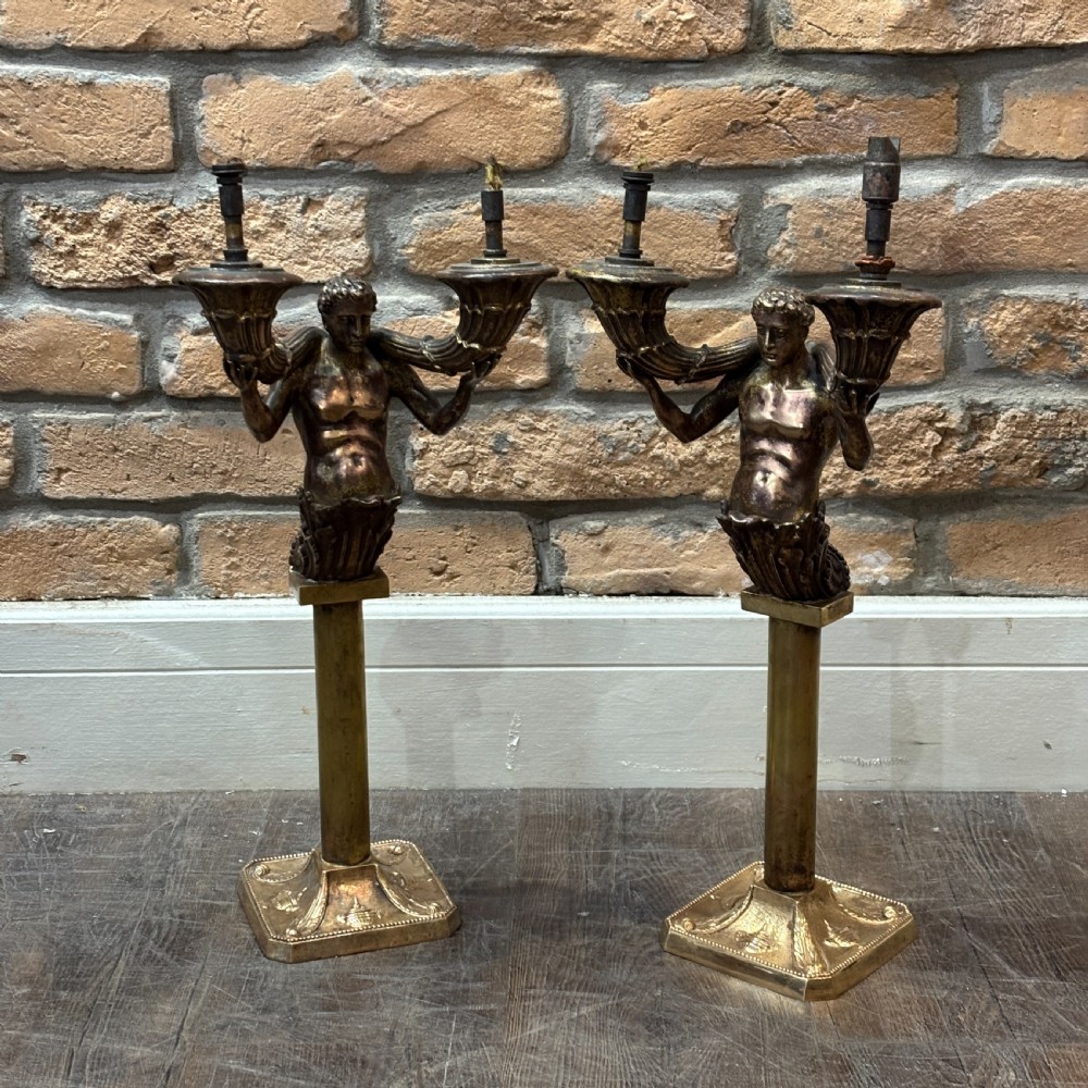 A pair of dark bronze Neoclassical table lamps featuring merman figures supporting twin cornucopia arms on square bases.