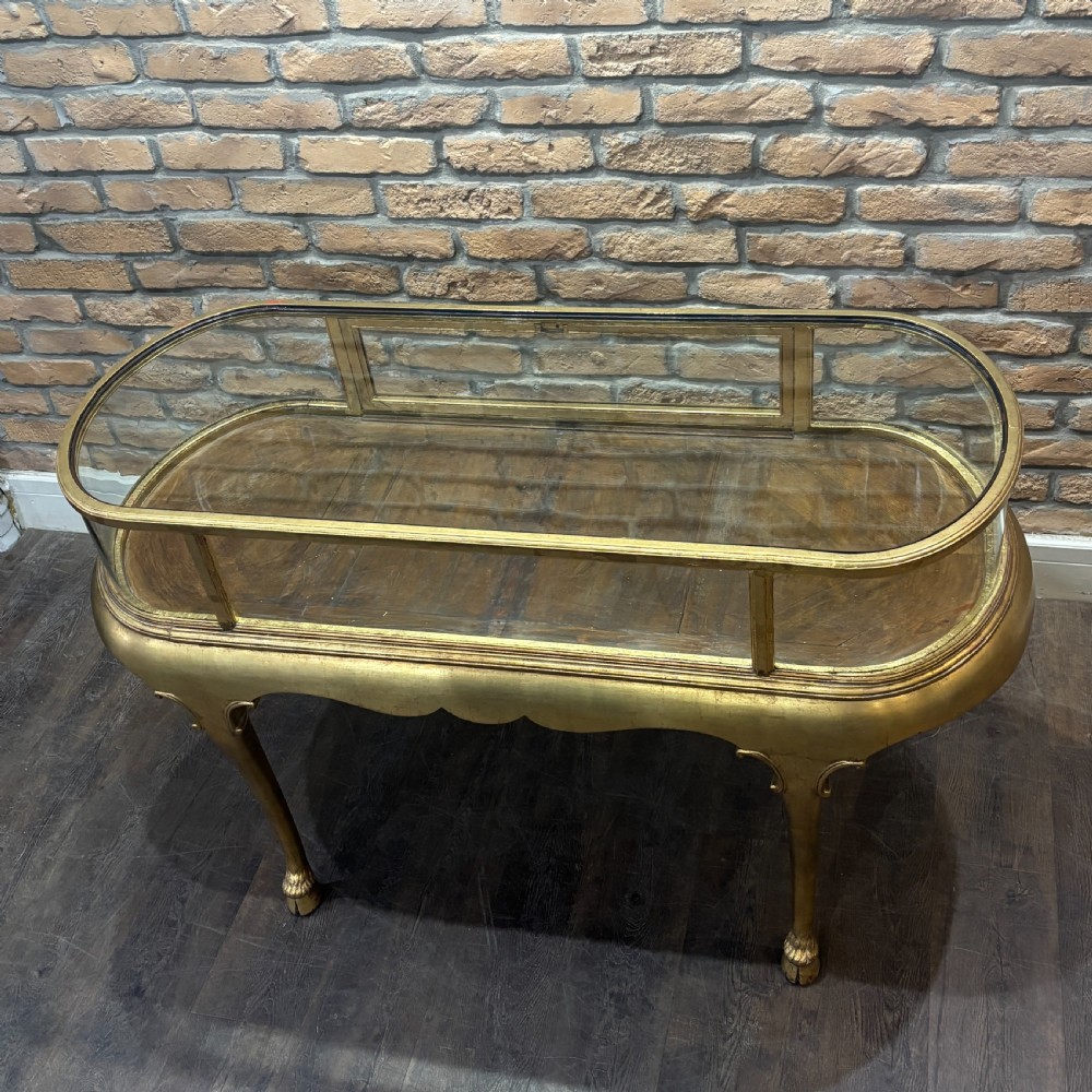 A gilded 1910s oval glass display counter featuring curved side panels and cabriole legs ending in hoof feet. View II