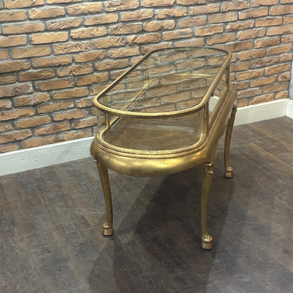 A gilded 1910s oval glass display counter featuring curved side panels and cabriole legs ending in hoof feet. View III