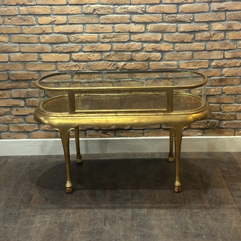 A gilded 1910s oval glass display counter featuring curved side panels and cabriole legs ending in hoof feet. View IV