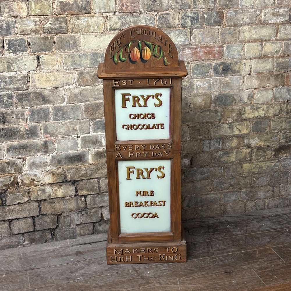 A tall, narrow mahogany advertising display cabinet featuring white glass panels with gold lettering for Frys Chocolate and an arched painted crest.