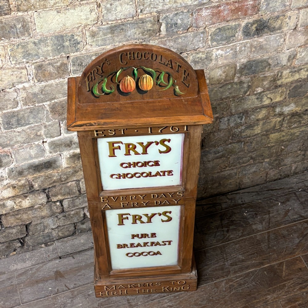 A tall, narrow mahogany advertising display cabinet featuring white glass panels with gold lettering for Frys Chocolate and an arched painted crest. View II