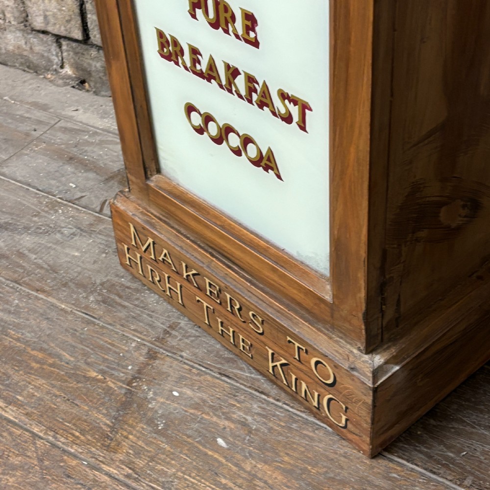 A tall, narrow mahogany advertising display cabinet featuring white glass panels with gold lettering for Frys Chocolate and an arched painted crest. View IV