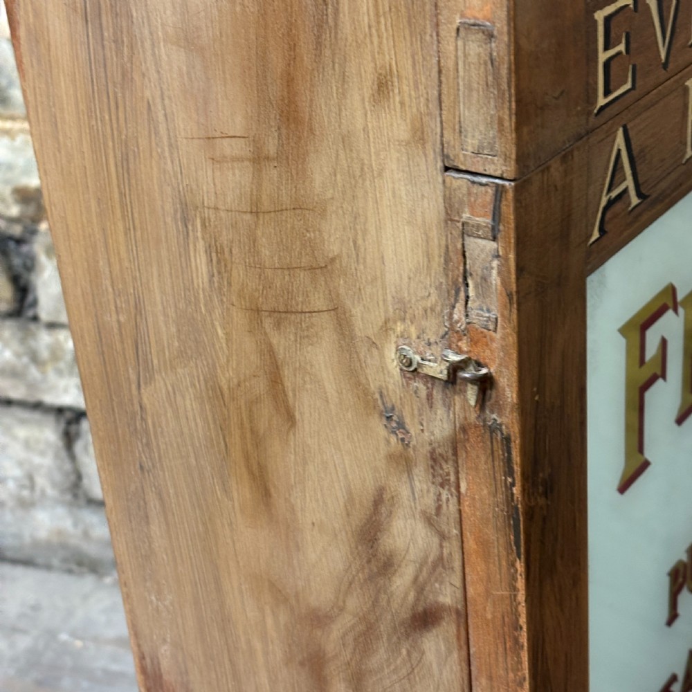 A tall, narrow mahogany advertising display cabinet featuring white glass panels with gold lettering for Frys Chocolate and an arched painted crest. View VI