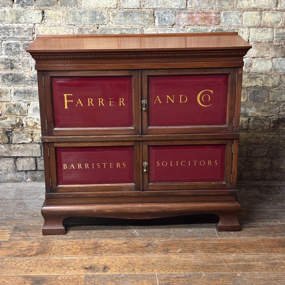 An early 20th-century mahogany office cabinet featuring four maroon panels with gold hand-lettering reading Farrer and Co Barristers Solicitors.