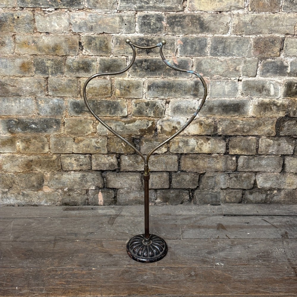 An early 20th-century brass drapers display stand featuring a wire bust frame on an adjustable central column with a heavy fluted cast iron base.
