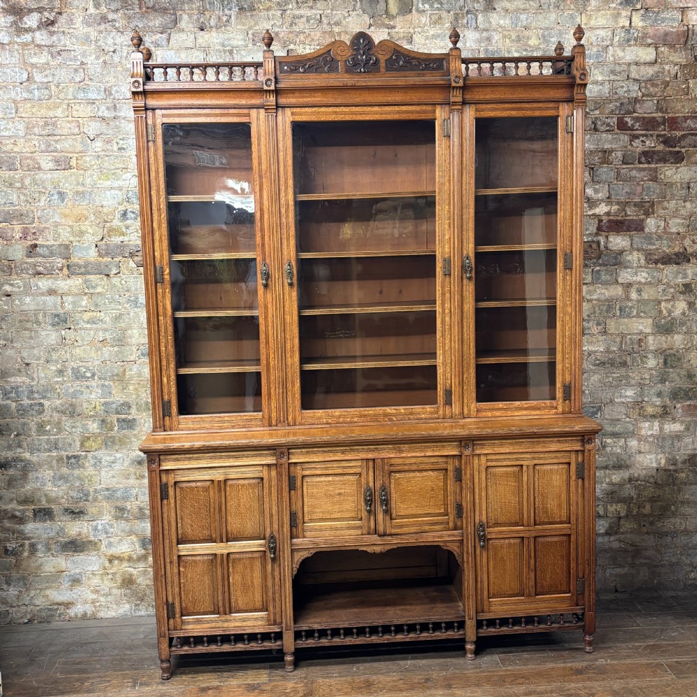 A large Victorian carved oak display cabinet featuring three glazed upper doors, a spindle gallery rail, and panelled lower cupboard doors.