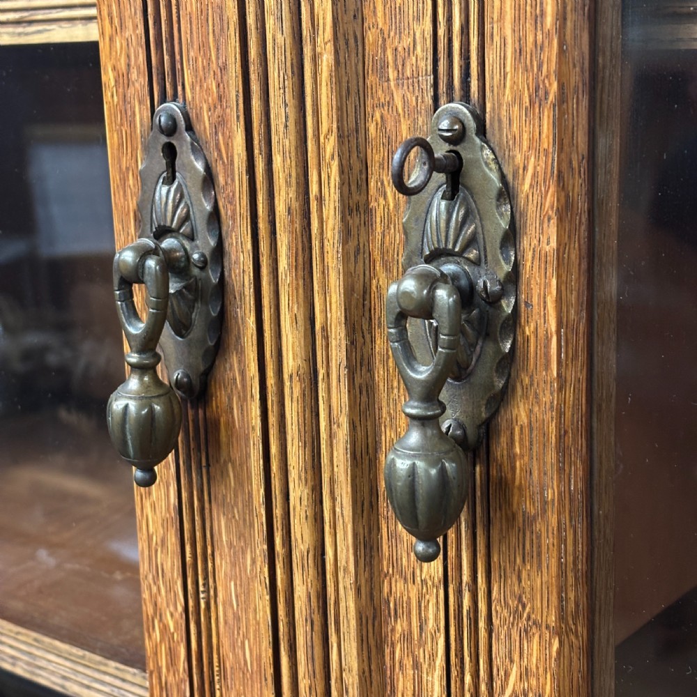 A large Victorian carved oak display cabinet featuring three glazed upper doors, a spindle gallery rail, and panelled lower cupboard doors. View IV