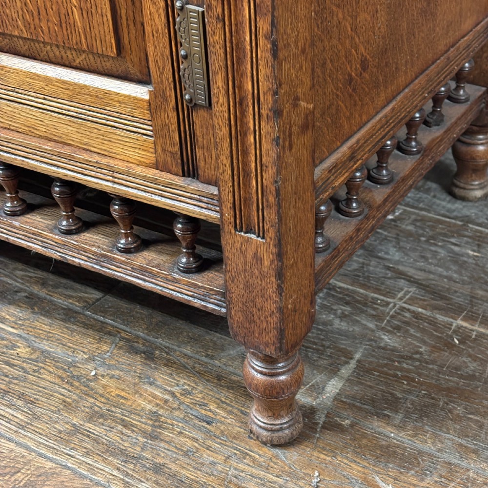 A large Victorian carved oak display cabinet featuring three glazed upper doors, a spindle gallery rail, and panelled lower cupboard doors. View VI