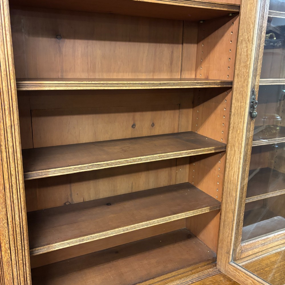 A large Victorian carved oak display cabinet featuring three glazed upper doors, a spindle gallery rail, and panelled lower cupboard doors. View VII