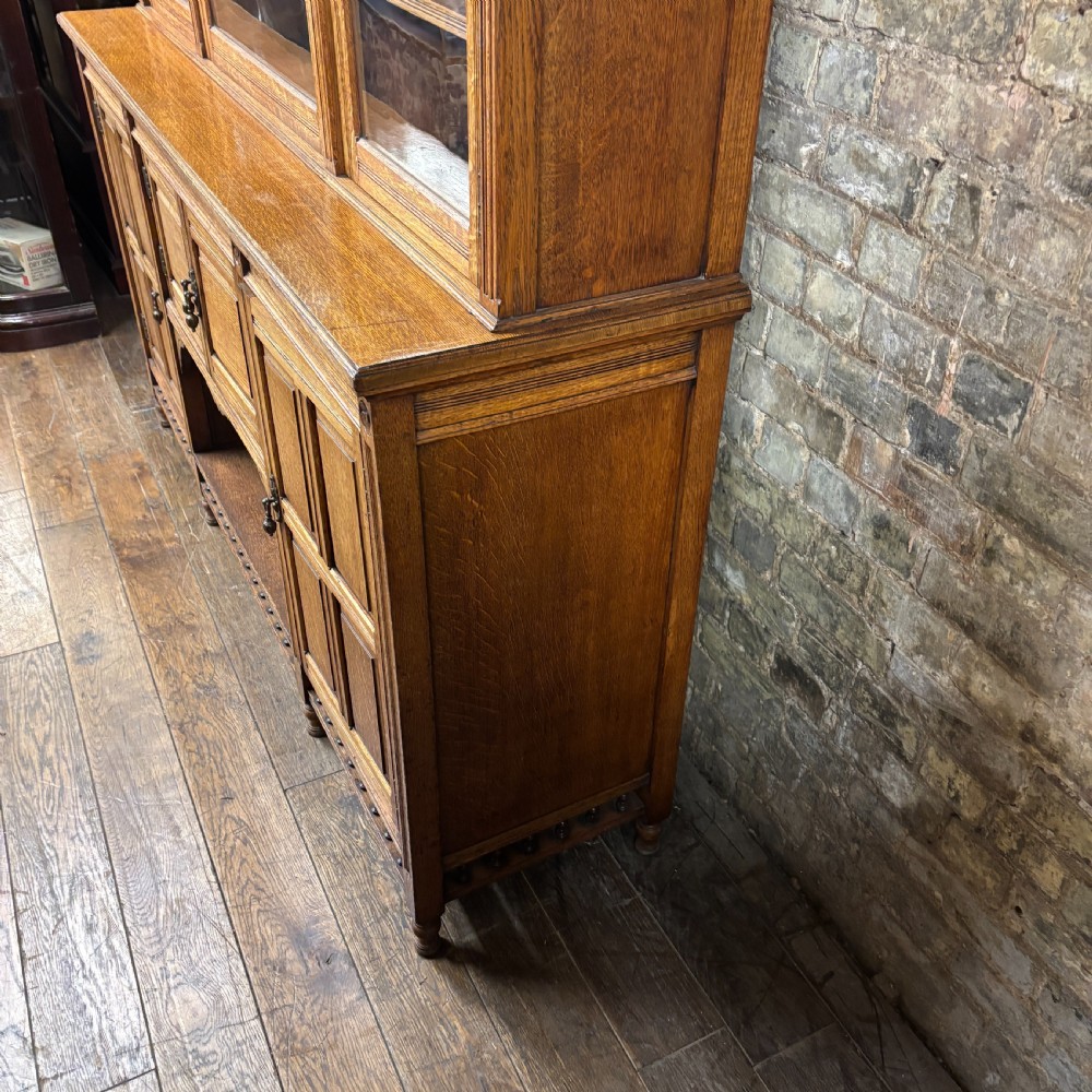 A large Victorian carved oak display cabinet featuring three glazed upper doors, a spindle gallery rail, and panelled lower cupboard doors. View IX