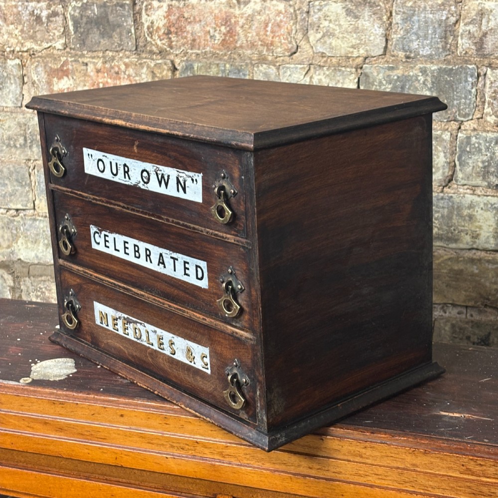A dark oak three-drawer tabletop drapers cabinet featuring hand-painted commercial typography and brass drop handles. View II