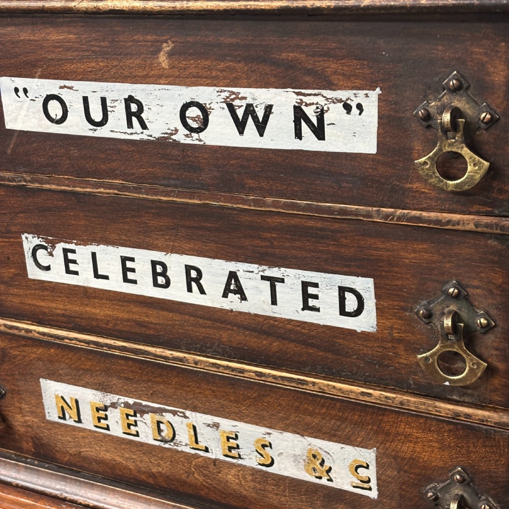 A dark oak three-drawer tabletop drapers cabinet featuring hand-painted commercial typography and brass drop handles. View III
