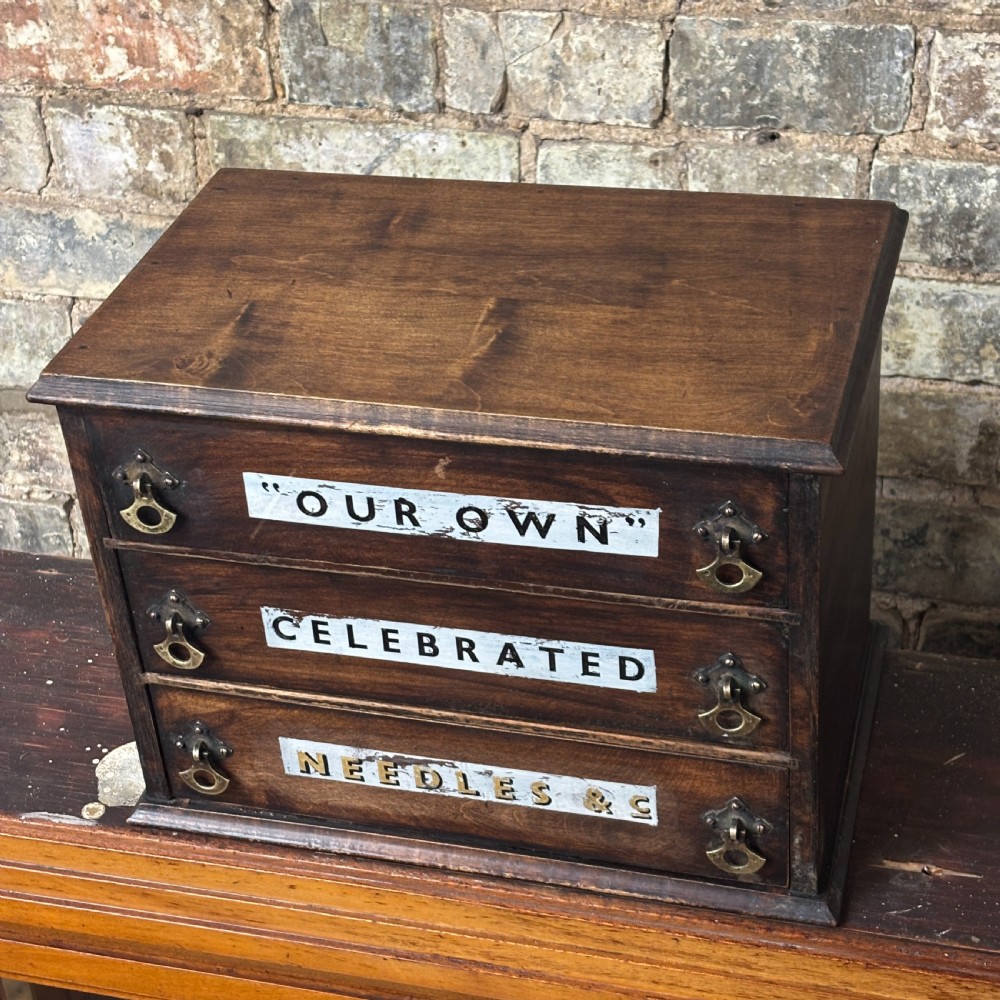 A dark oak three-drawer tabletop drapers cabinet featuring hand-painted commercial typography and brass drop handles. View IV