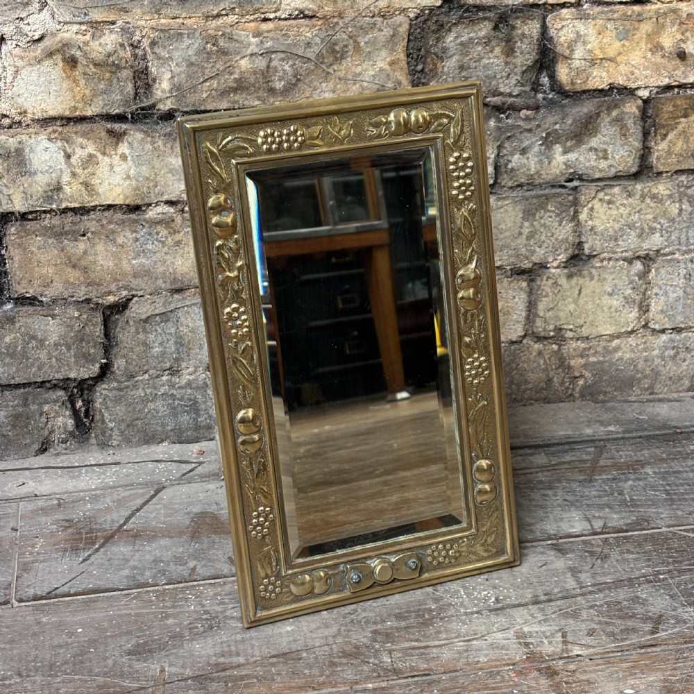 A rectangular Edwardian dressing table mirror with an embossed brass frame featuring fruit motifs surrounding bevelled mirror glass.