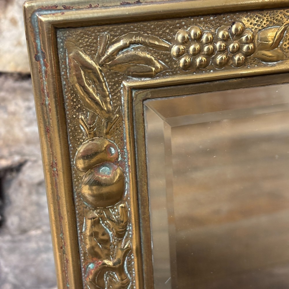 A rectangular Edwardian dressing table mirror with an embossed brass frame featuring fruit motifs surrounding bevelled mirror glass. View IV