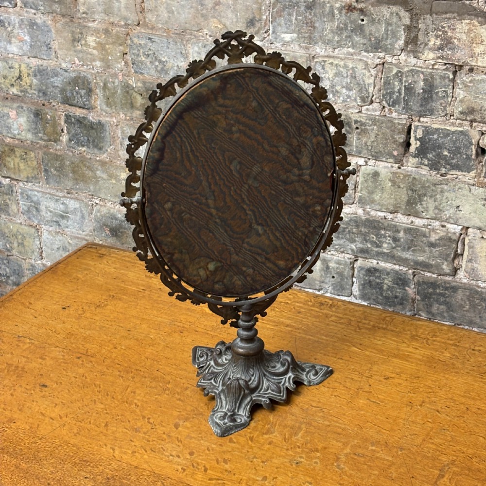 A late Victorian cast bronze dressing table mirror featuring an oval glass frame adorned with intricate floral scrollwork set upon an ornate pedestal base. View III