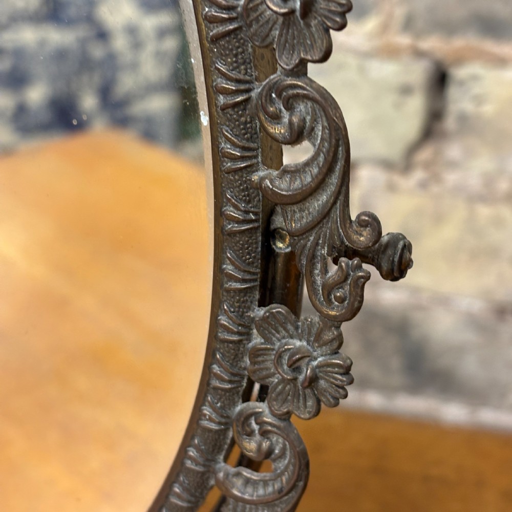 A late Victorian cast bronze dressing table mirror featuring an oval glass frame adorned with intricate floral scrollwork set upon an ornate pedestal base. View VI