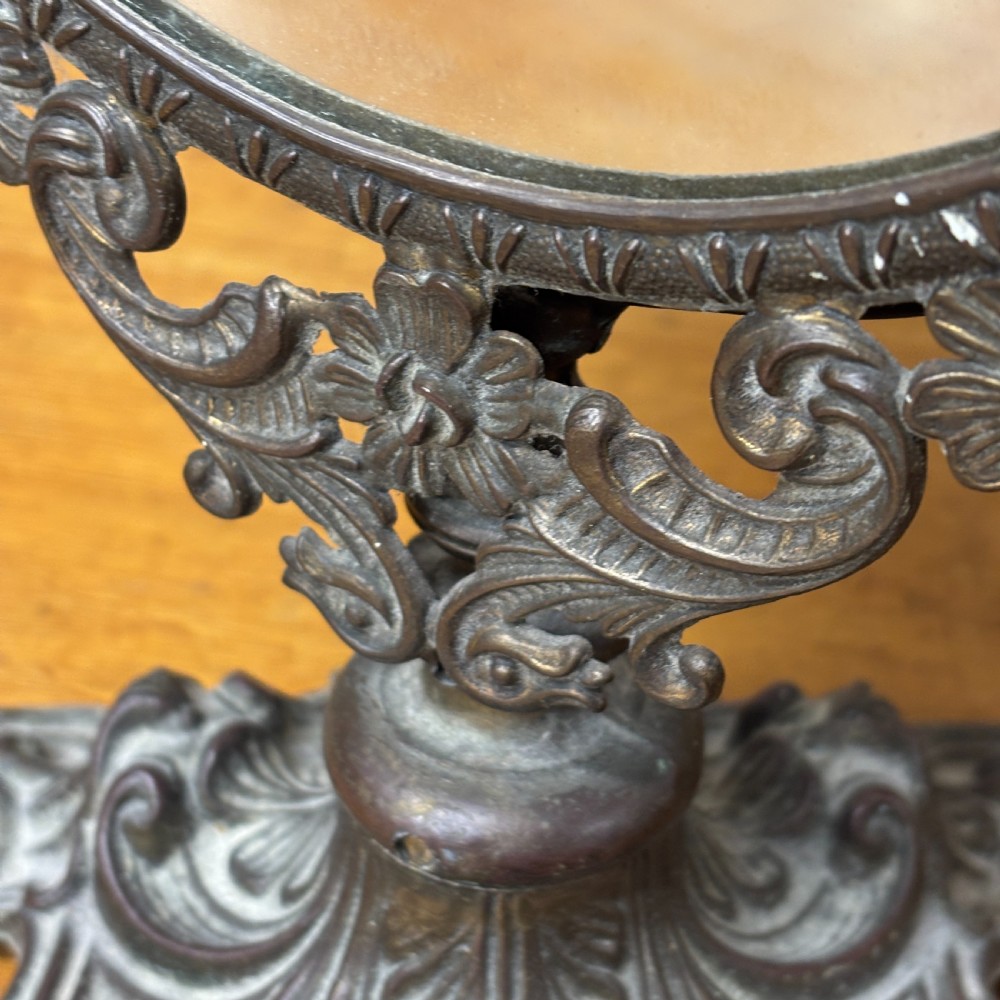 A late Victorian cast bronze dressing table mirror featuring an oval glass frame adorned with intricate floral scrollwork set upon an ornate pedestal base. View VII