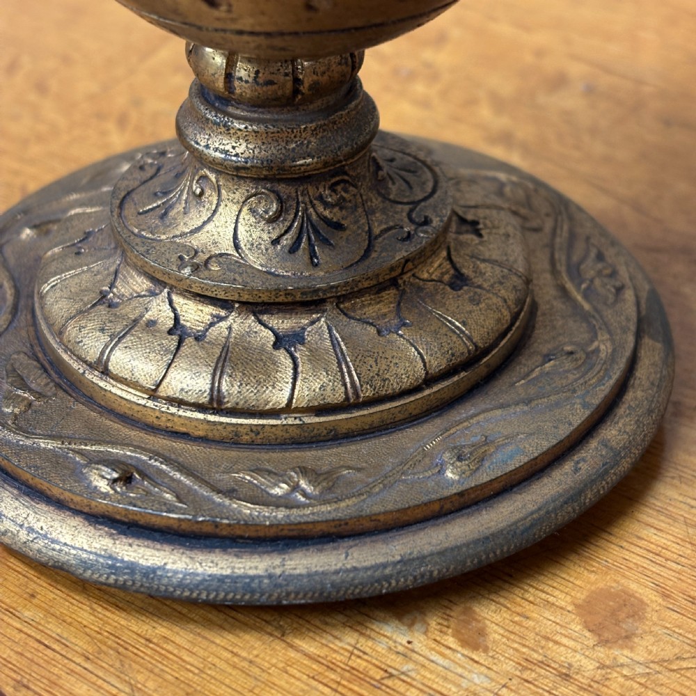 An antique cast brass candlestick featuring an urn-shaped central section with relief mask details, a stepped turned stem, and a fluted nozzle. View II