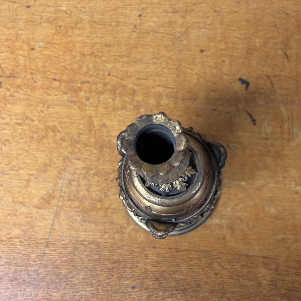 An antique cast brass candlestick featuring an urn-shaped central section with relief mask details, a stepped turned stem, and a fluted nozzle. View VI