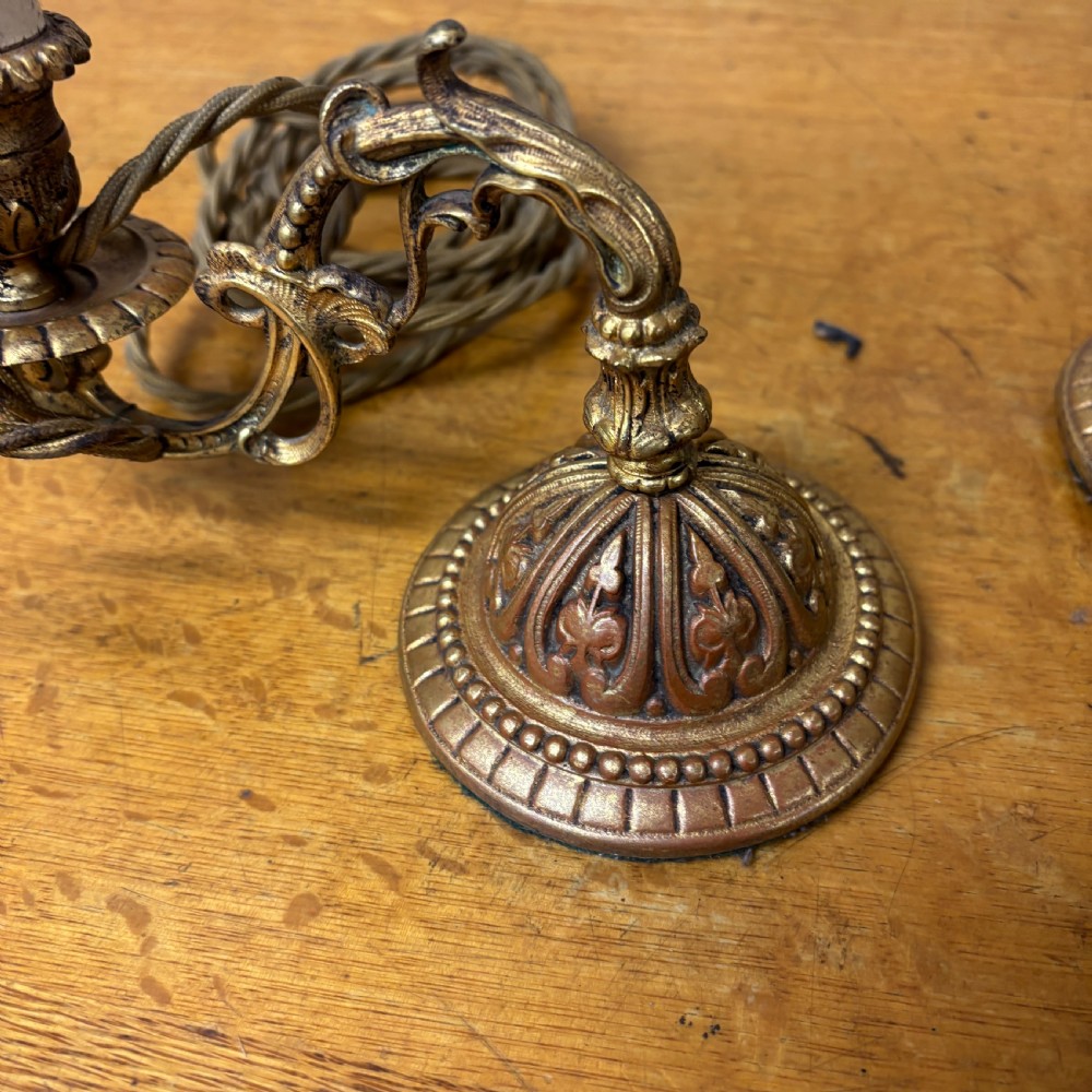 A pair of early 20th-century cast brass wall sconces featuring ornate scrollwork arms, gadrooned backplates, and cream-coloured candle sleeves. View III