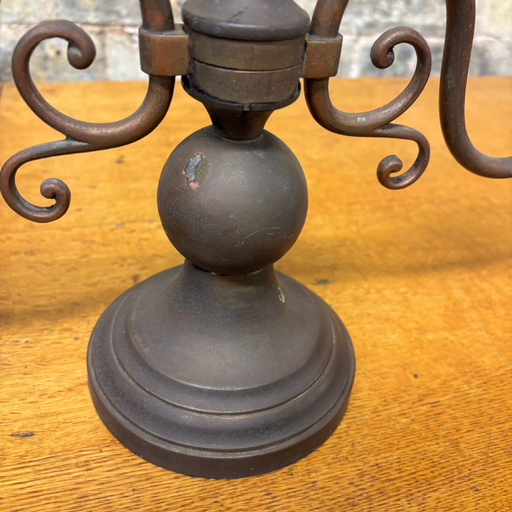 An early 20th-century patinated brass two-arm candelabra table lamp featuring curved scroll arms, faux candle sleeves, and a stepped circular base. View III