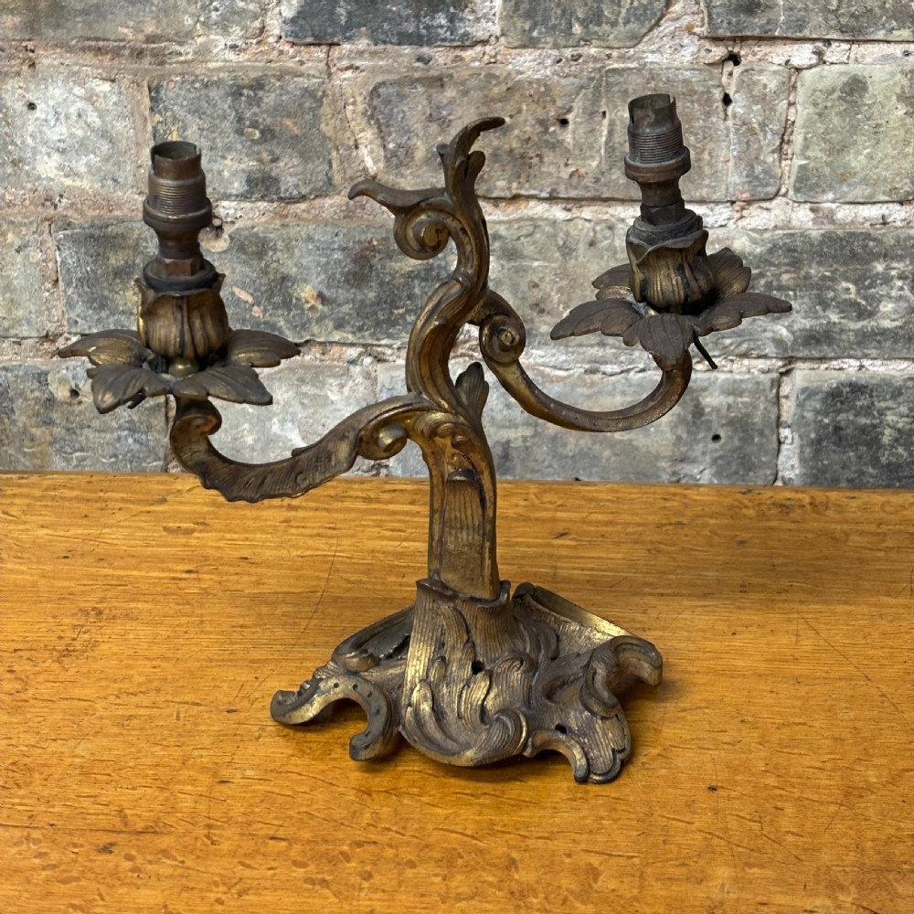 A two-arm gilt brass table lamp base featuring sculpted leaf motifs, curved organic branches, and a broad scrolling base.