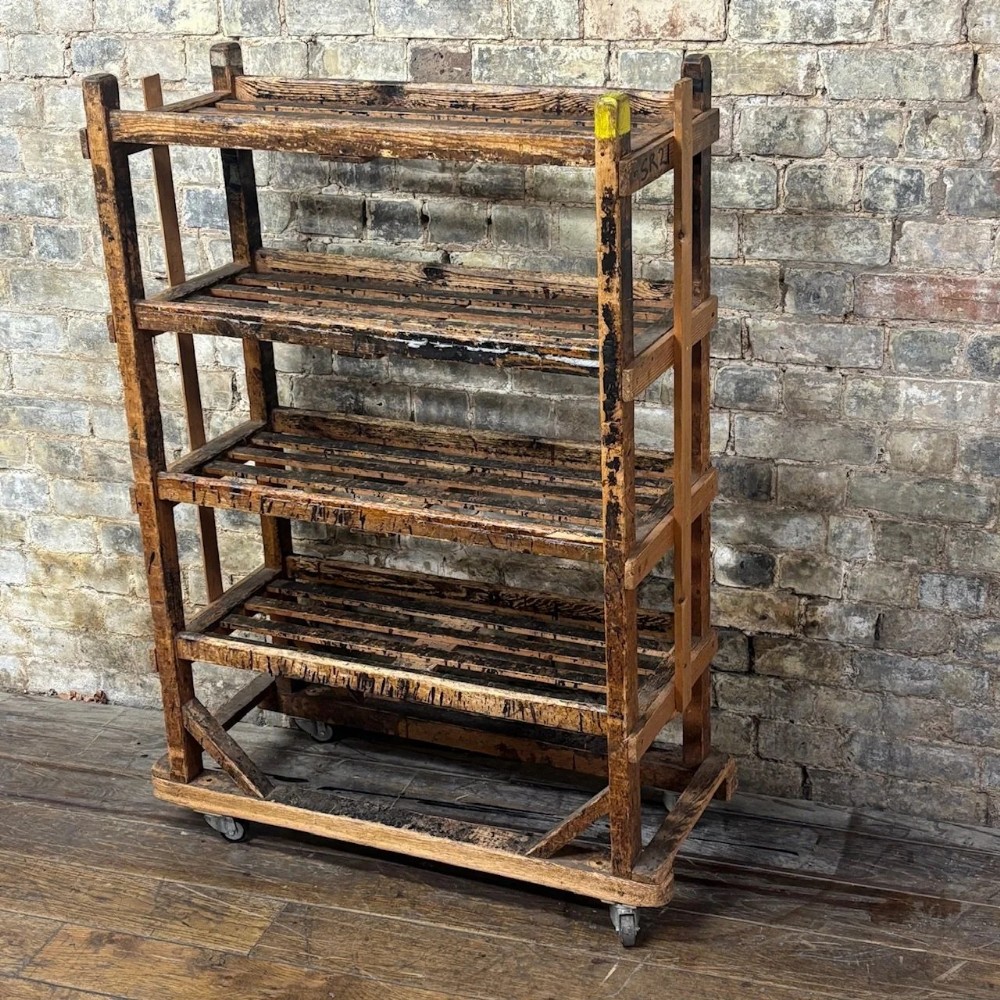 A four-tiered early 20th-century wooden shoe trolley featuring slatted pine shelves, diagonal corner bracing, and metal swivel castors at the base.