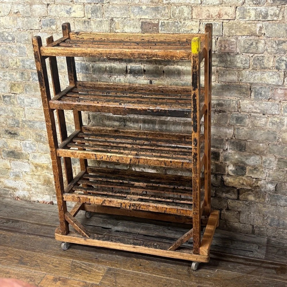 An early 20th-century four-tier wooden industrial shoe trolley with slatted shelves and small metal castor wheels at the base.