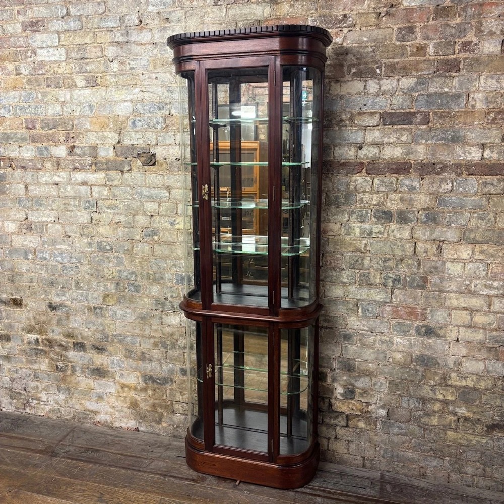A tall Edwardian mahogany two-part display cabinet with curved glass sides, glazed doors, adjustable glass shelves, and brass escutcheons.