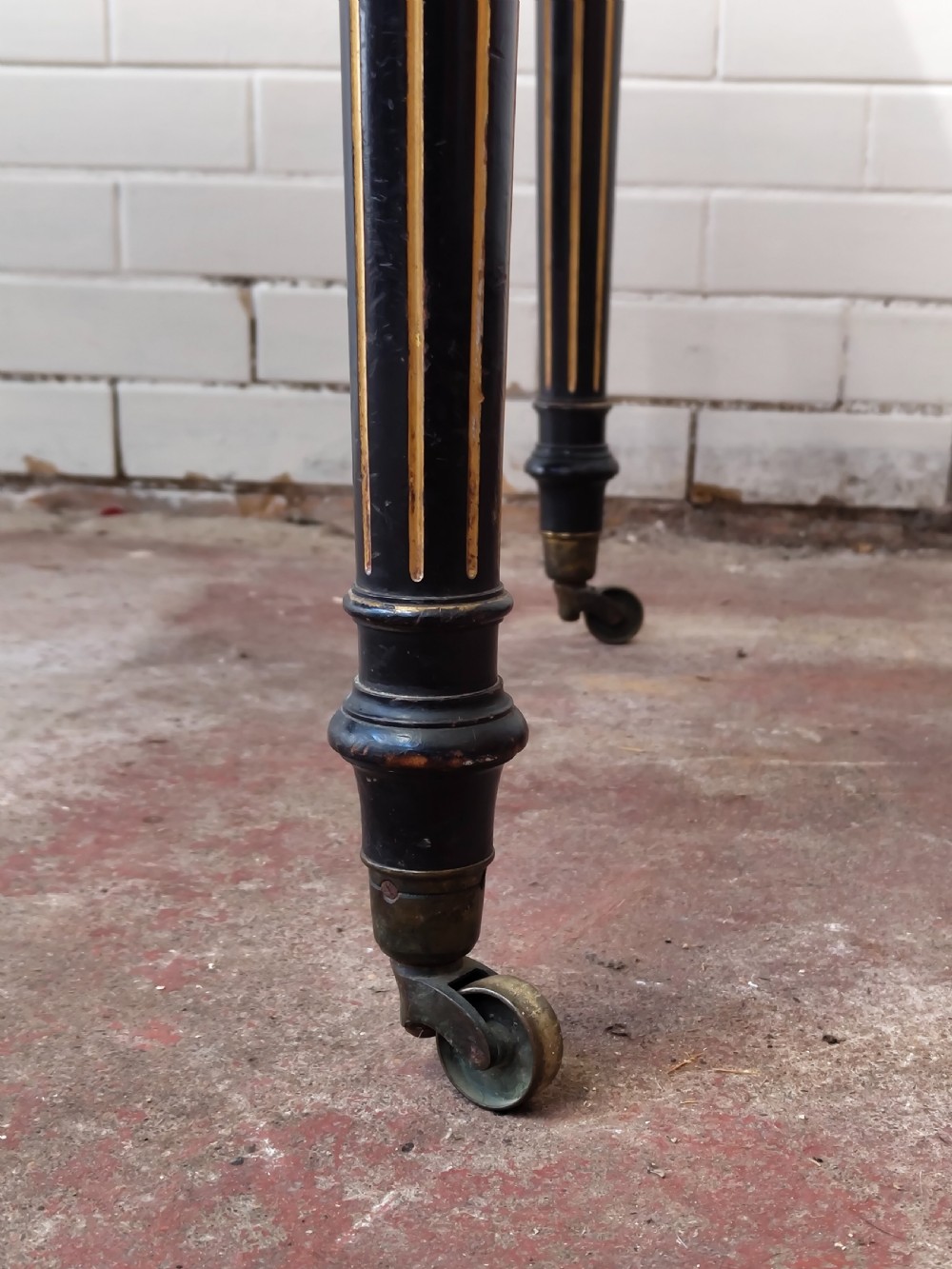 A Victorian Aesthetic Movement ebonised writing table featuring a brown leather inset top, fluted legs with gilt detailing, and brass castors. View XII