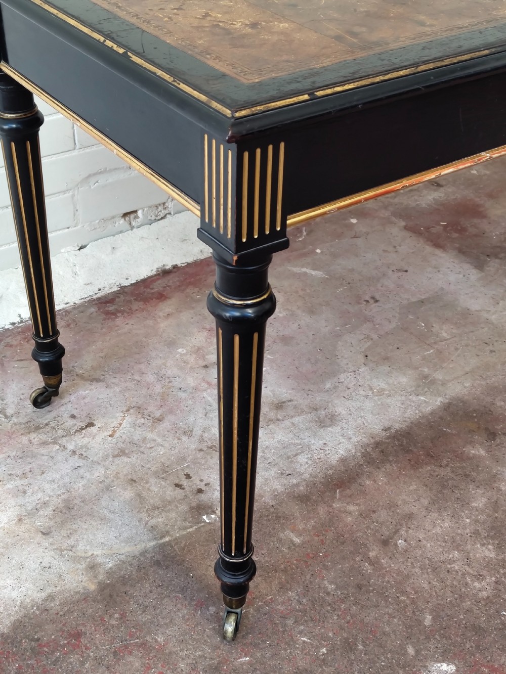 A Victorian Aesthetic Movement ebonised writing table featuring a brown leather inset top, fluted legs with gilt detailing, and brass castors. View III