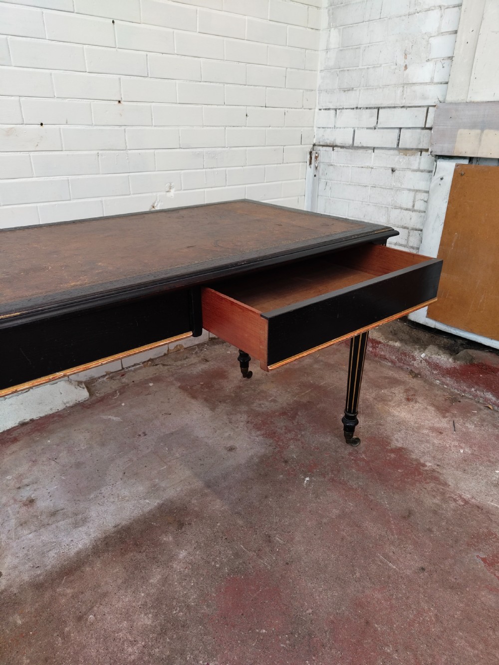 A Victorian Aesthetic Movement ebonised writing table featuring a brown leather inset top, fluted legs with gilt detailing, and brass castors. View VI