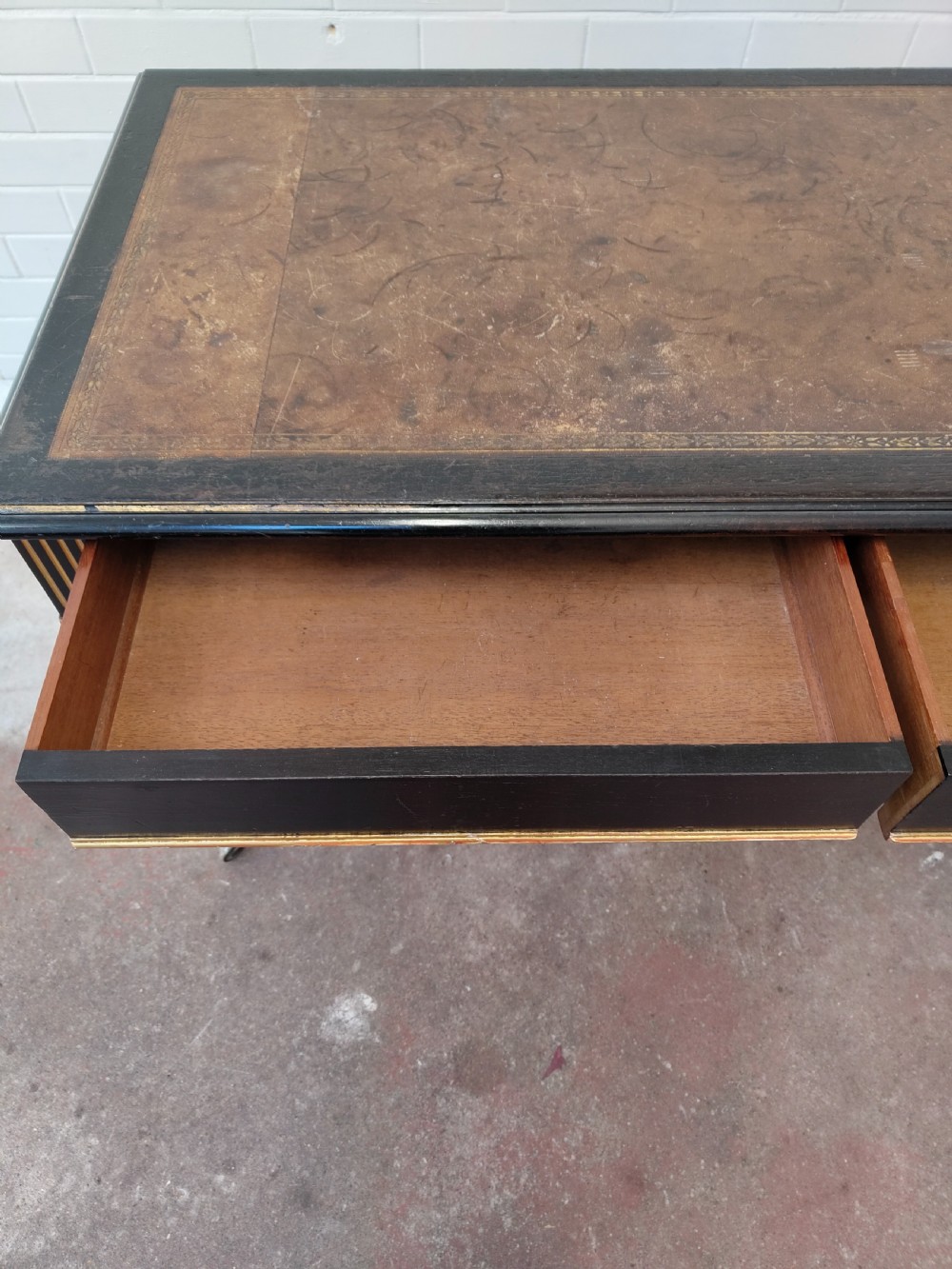 A Victorian Aesthetic Movement ebonised writing table featuring a brown leather inset top, fluted legs with gilt detailing, and brass castors. View VII