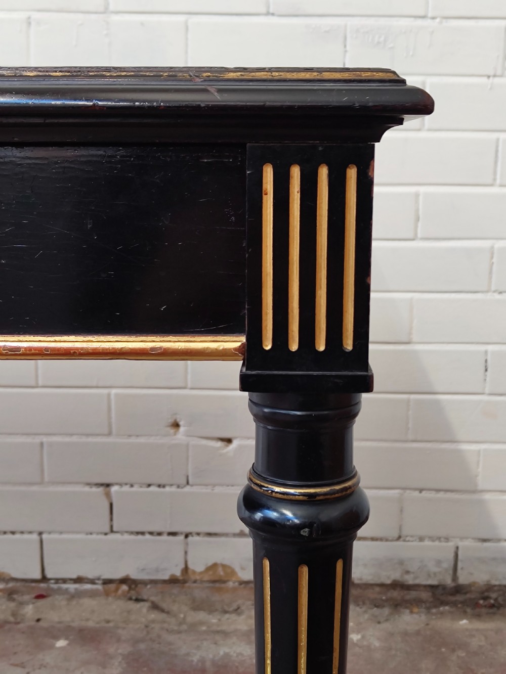 A Victorian Aesthetic Movement ebonised writing table featuring a brown leather inset top, fluted legs with gilt detailing, and brass castors. View VIII